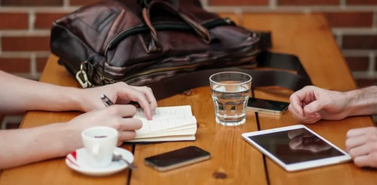 twee personen zitten tegenover elkaar aan een tafel waarvan een in een boekje schrijft