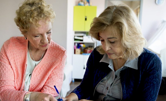 Zittend aan tafel helpt een medewerkster een vrouw bij het indienen van een aanvraag.