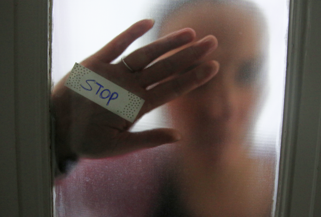 Hand tegen raam, met het woord 'stop'.